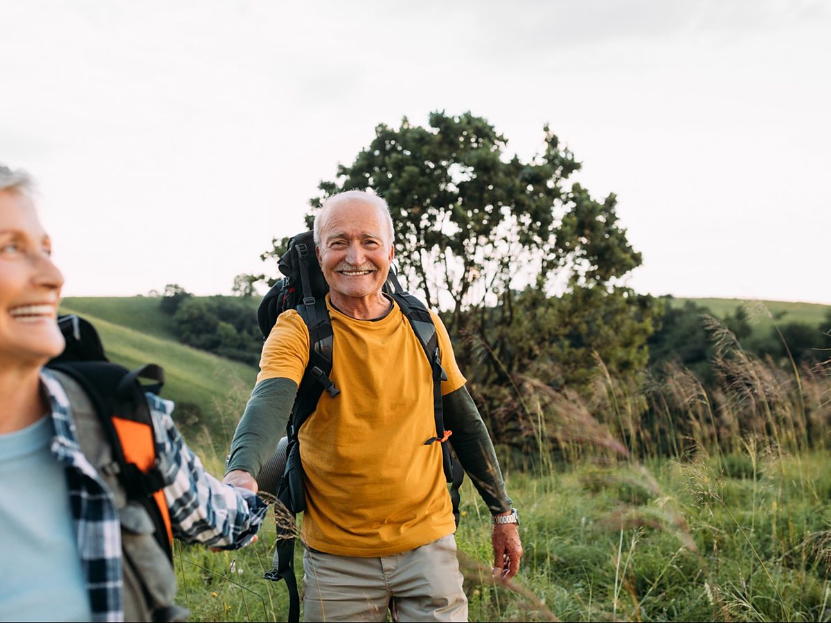 A couple hikes through green hills with backpacks