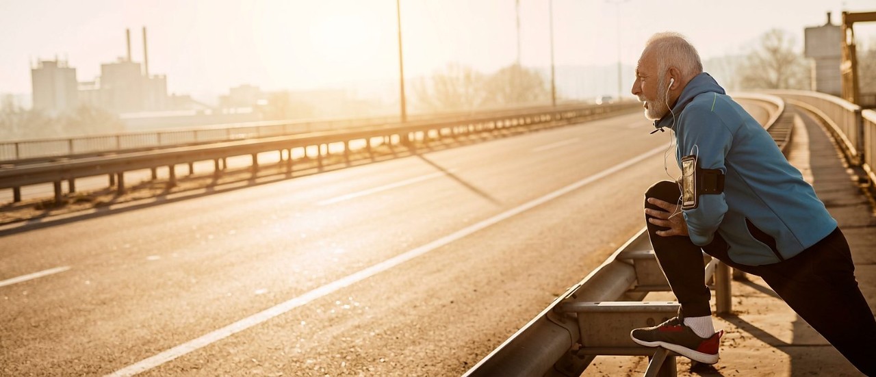 A man stretches on a bridge railing at sunrise