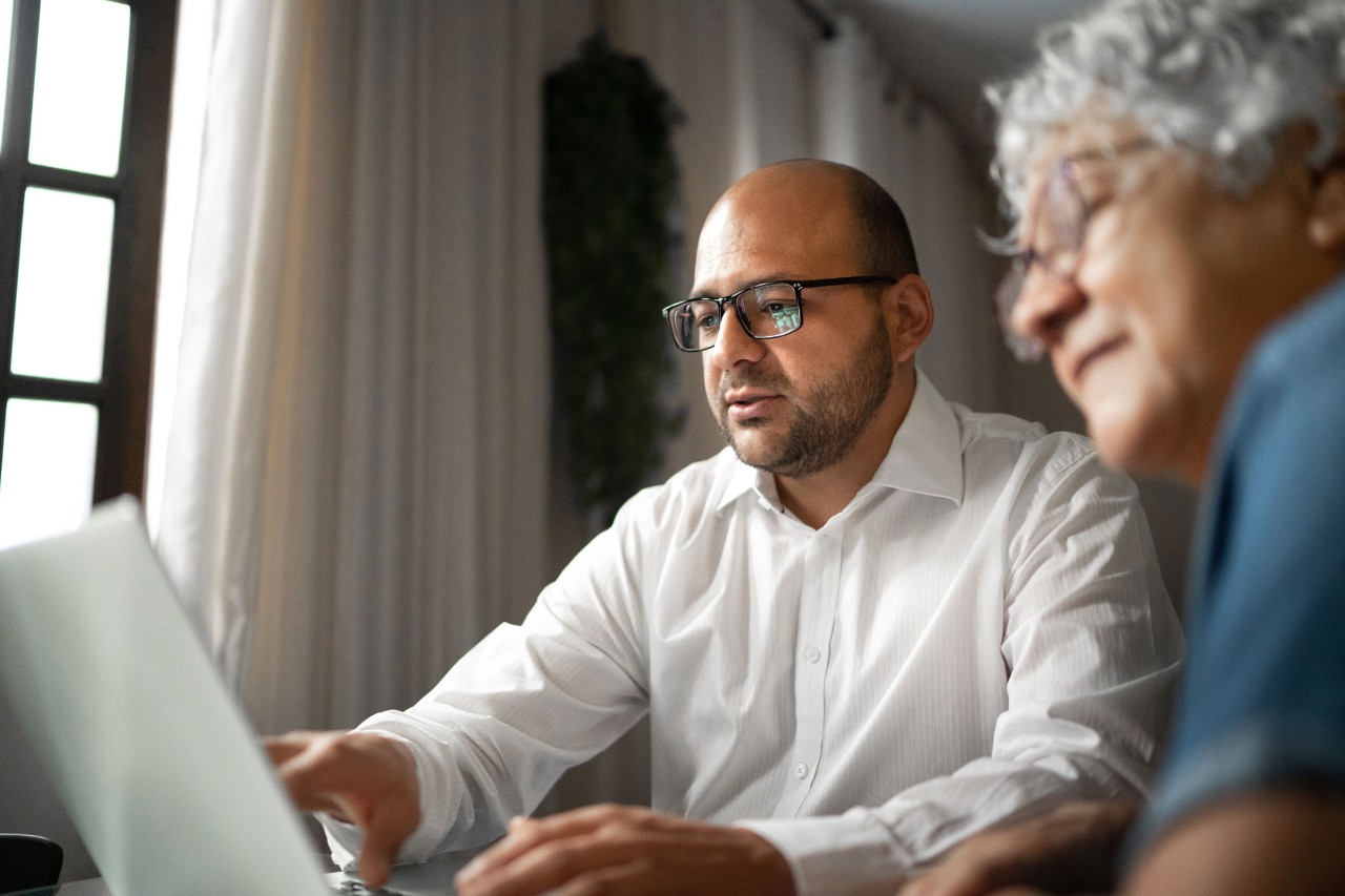 An advisor in glasses works through a plan on a laptop with an older client