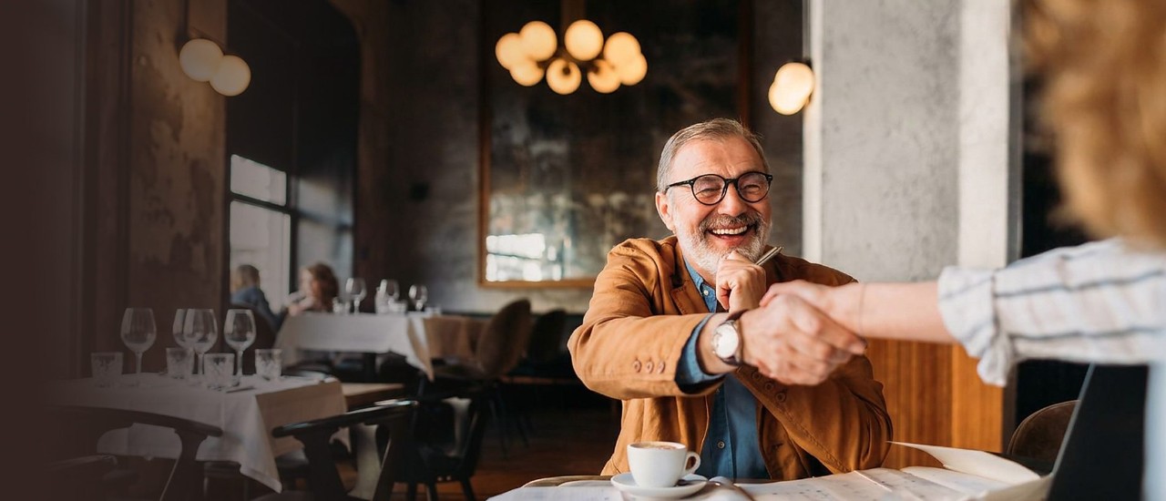A laughing man shakes hands across a cafe table