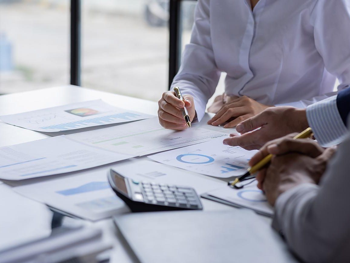Hands with pens review printed financial charts beside a calculator